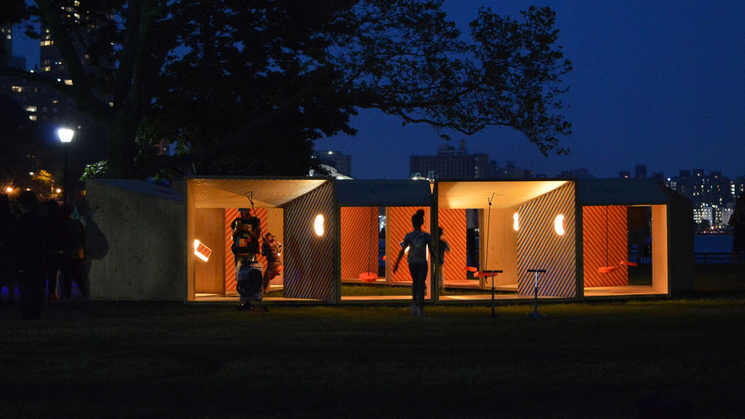 Picture of the "Salvage Swings" project lit up at night time, with a few people interacting with the project
