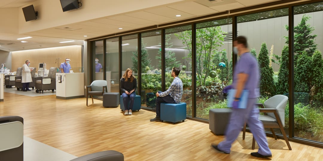 people sitting and walking in a clinic waiting are with views of a garden outside the windows