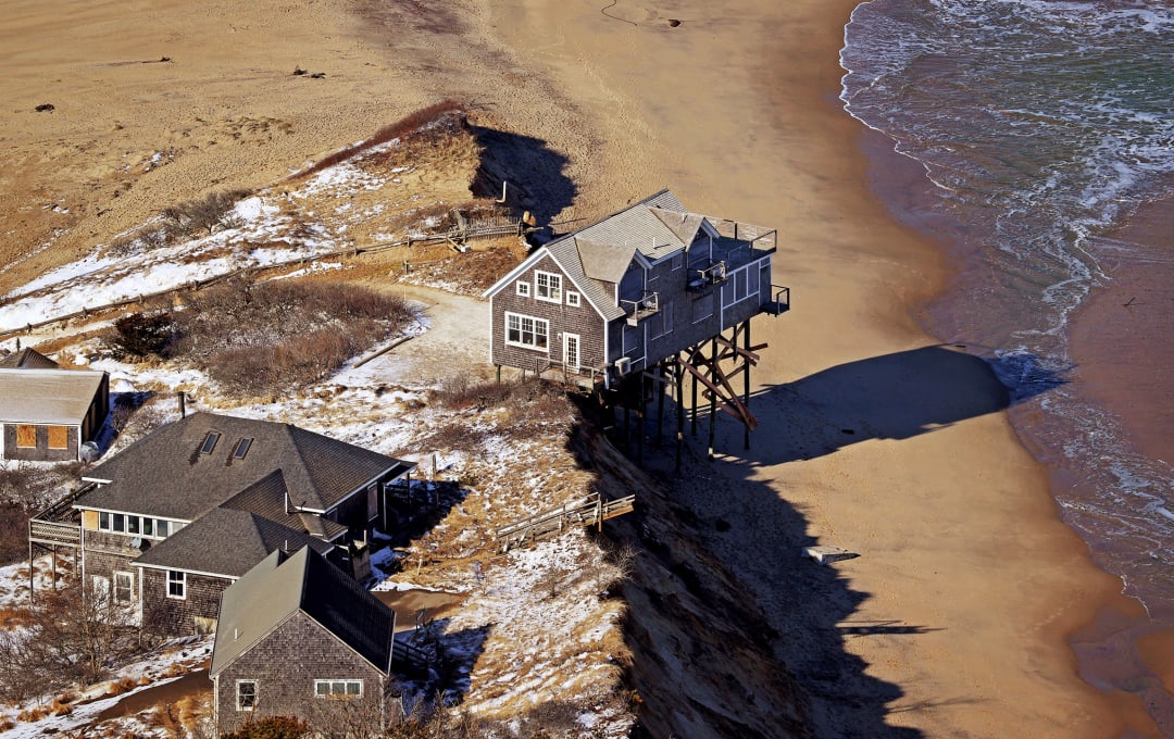 A coastal house on stilts sits on the edge of collapse after a storm in Mass.