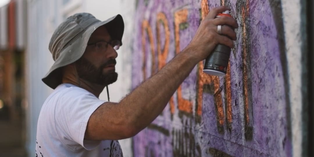 man spray painting the word "dream" on a concrete wall