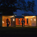 Picture of the "Salvage Swings" project lit up at night time, with a few people interacting with the project