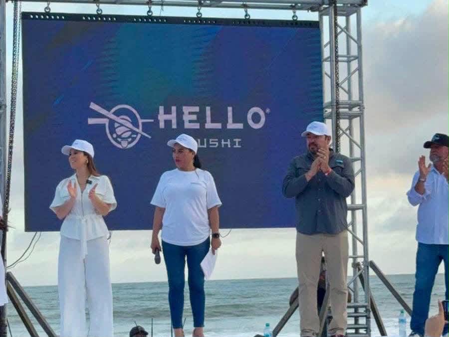 Participantes en el escenario frente al mar con el logotipo de Hello Sushi en pantalla