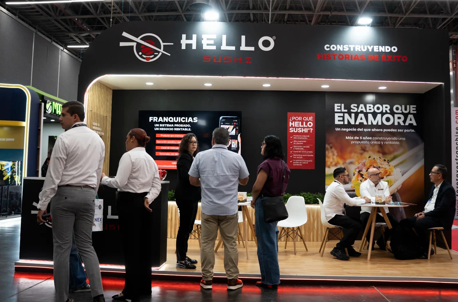 Visitantes conversan frente al muro de franquicias del stand de Hello Sushi