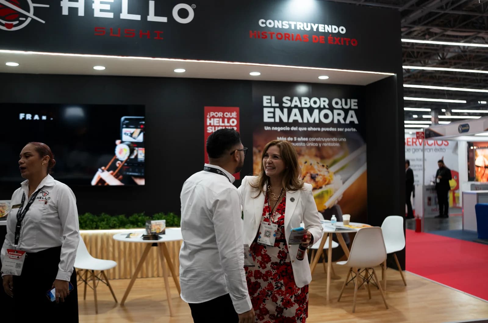 El equipo de Hello Sushi atiende a un visitante frente a la pantalla del stand