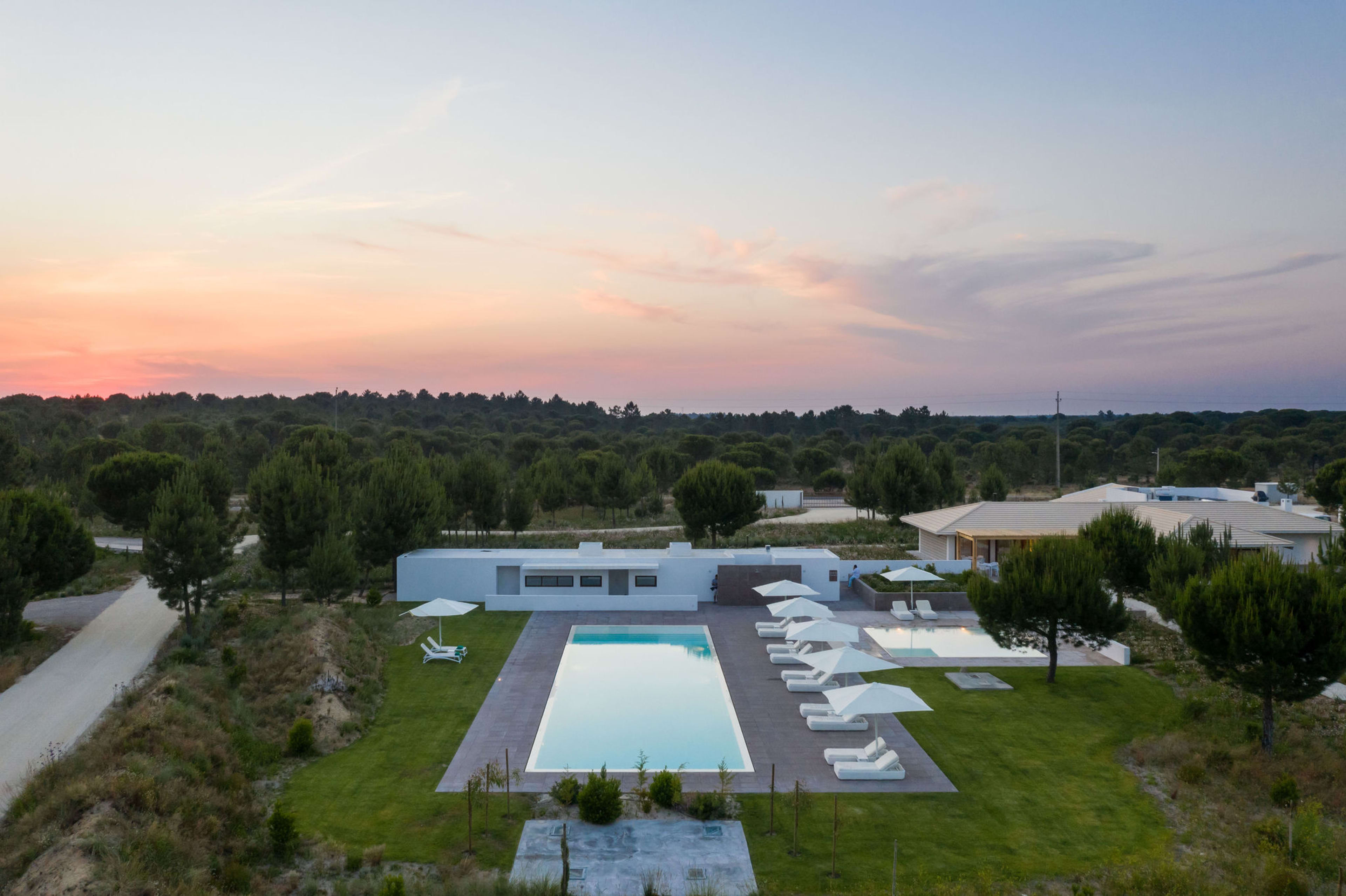 The estate from above at dusk — pool, pavilions and pine forest