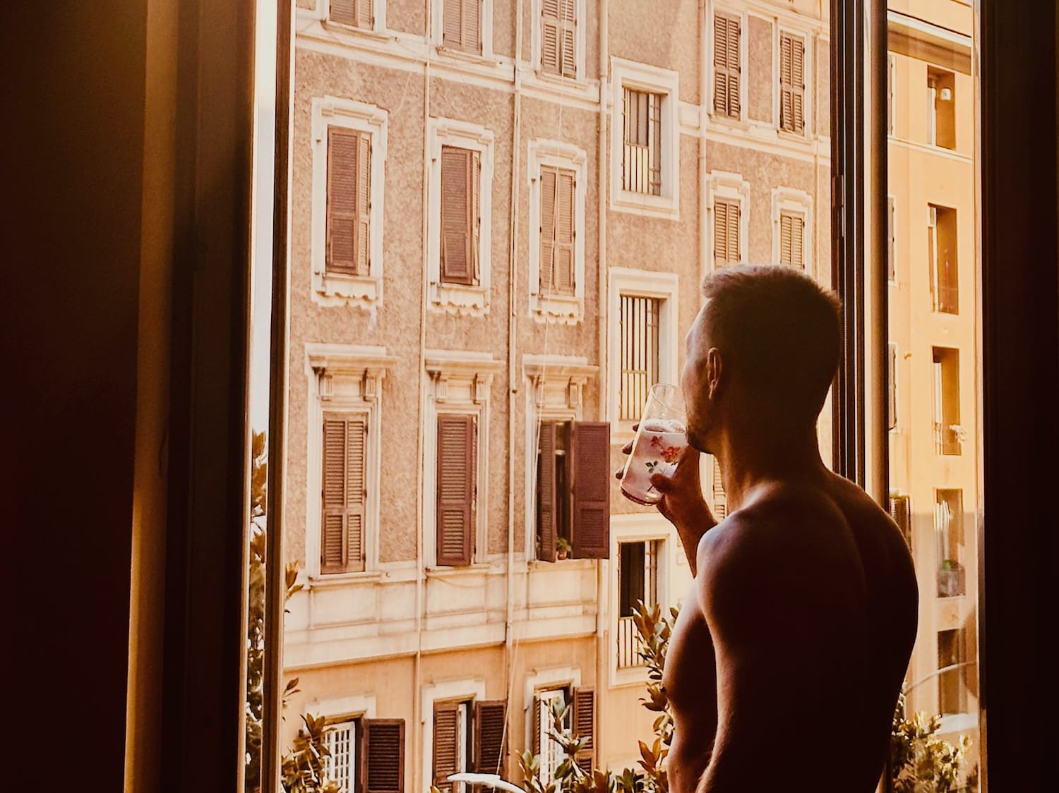 Man enjoying a morning view in gay Rome, looking out of an open window towards classic Roman architecture, capturing the serene atmosphere of the city.