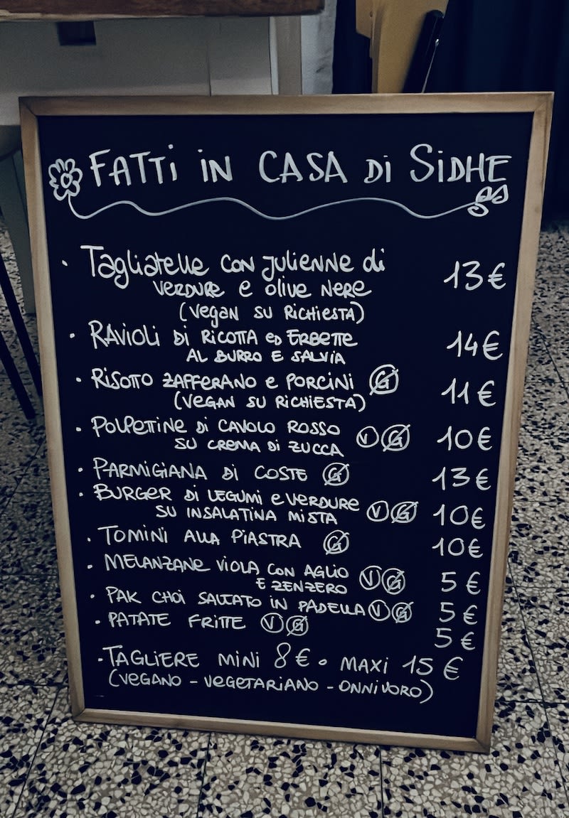 Chalkboard menu outside a restaurant in Milan featuring homemade Italian dishes with vegan and vegetarian options highlighted.