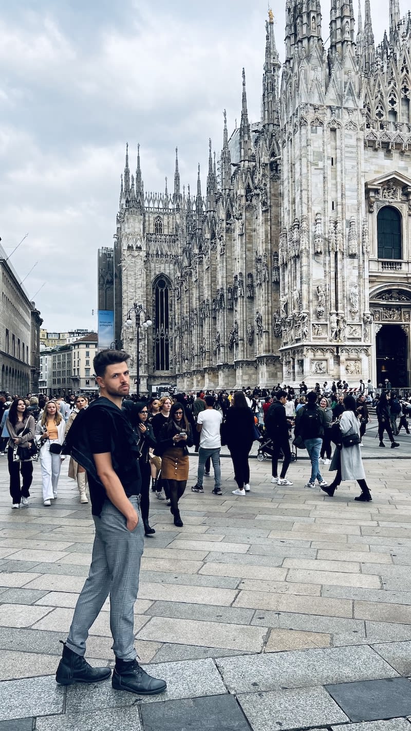 Man in casual attire walking in front of the crowded Milan Cathedral, showcasing the intricate Gothic architecture.