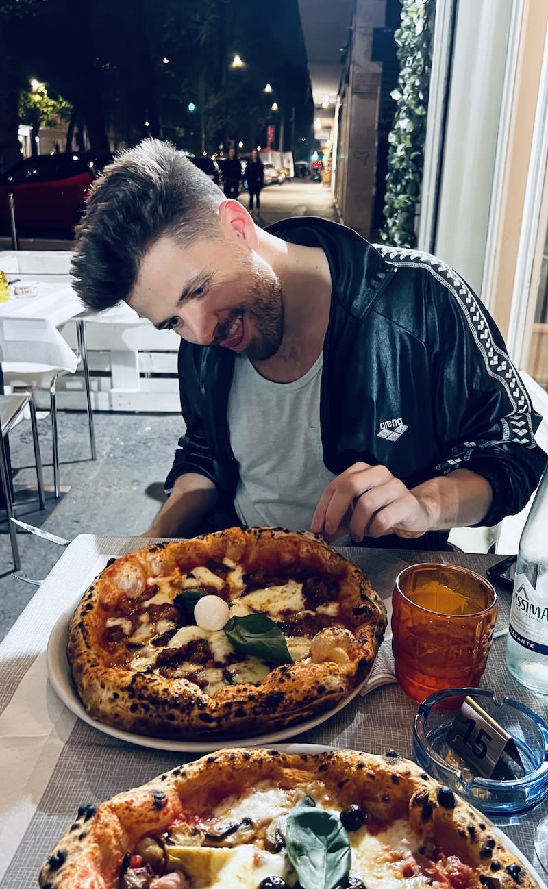 Cheerful man enjoying a freshly baked pizza at an outdoor restaurant in Milan, evoking a lively Italian dining experience.