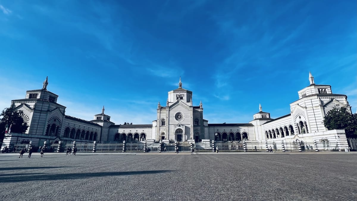 Panoramic view of a spacious public square in Milan with a grand museum building under a vivid blue sky, symbolizing Milan's cultural richness.