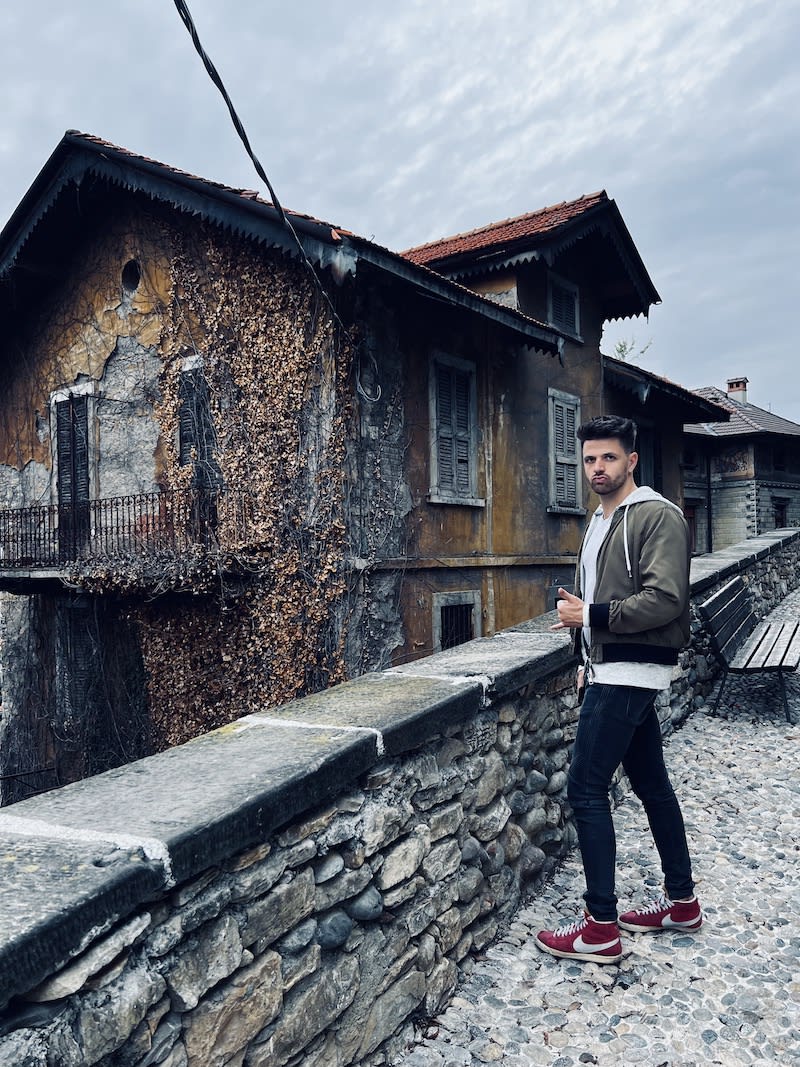 A man acting silly in front of a home in Bergamo with an dark overcast sky