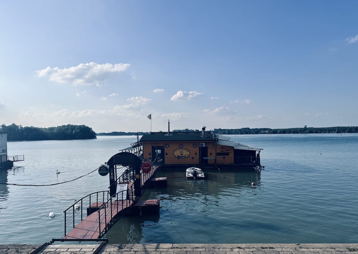 A floating bar on the Sava River in Belgrade, known as a 'splav,' with a connected walkway and serene water views. The bar is a popular spot for relaxation and socializing, particularly among the gay community