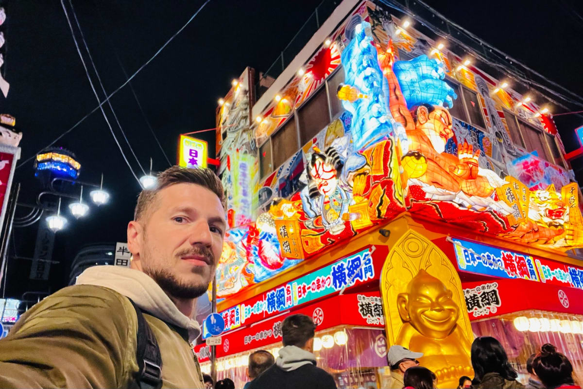 A vibrant night scene at Dotombori Market in Osaka, Japan, featuring brightly lit signs and a bustling street filled with people. This lively market is a highlight of any Honshu Japan itinerary, known for its food stalls and entertainment.