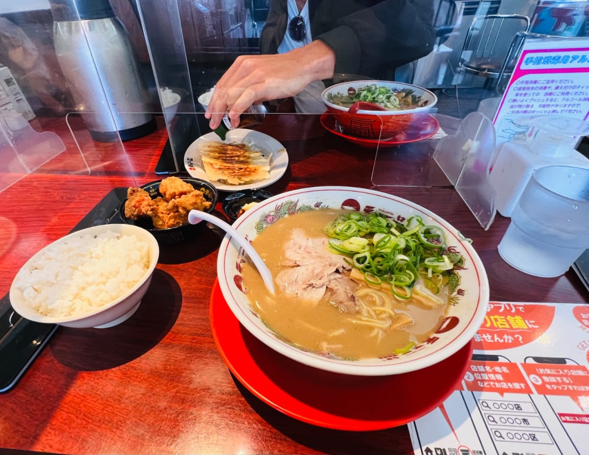 A table set with bowls of ramen, gyoza, fried chicken, and rice in a cozy Osaka ramen restaurant. Sampling local cuisine like this is an essential part of a culinary adventure on a Honshu Japan itinerary.