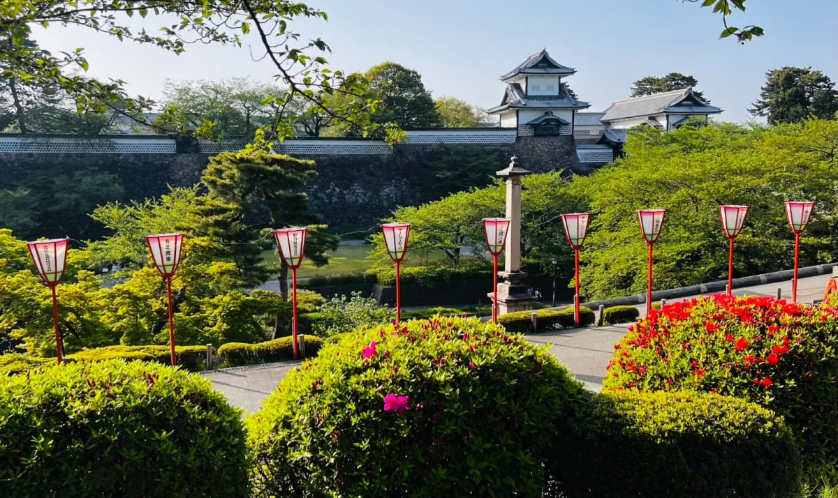 A picturesque view of Kanazawa Garden with meticulously trimmed bushes, lanterns, and the castle walls in the distance. This serene garden is a highlight on a Honshu Japan itinerary, perfect for a peaceful stroll.