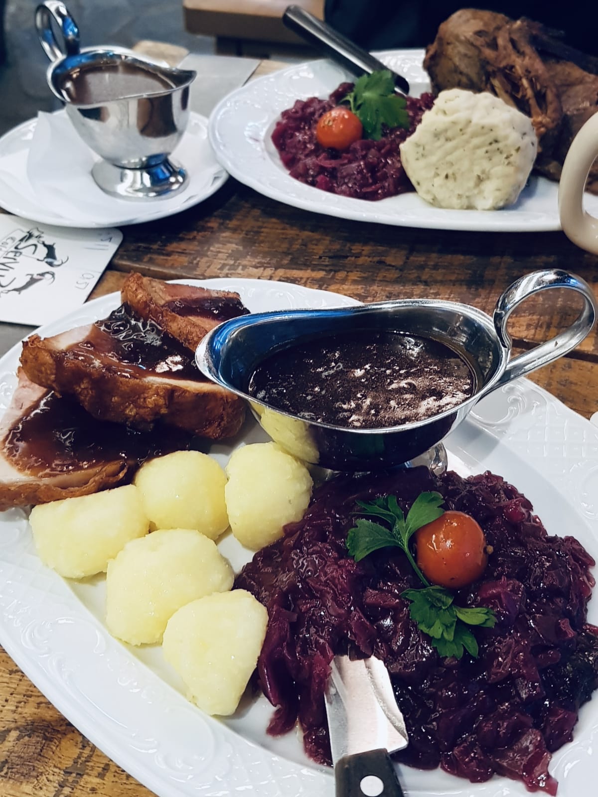 A German dinner featuring suckling roast pork belly, red cabbage, and boiled potatoes - with a gravy on the side