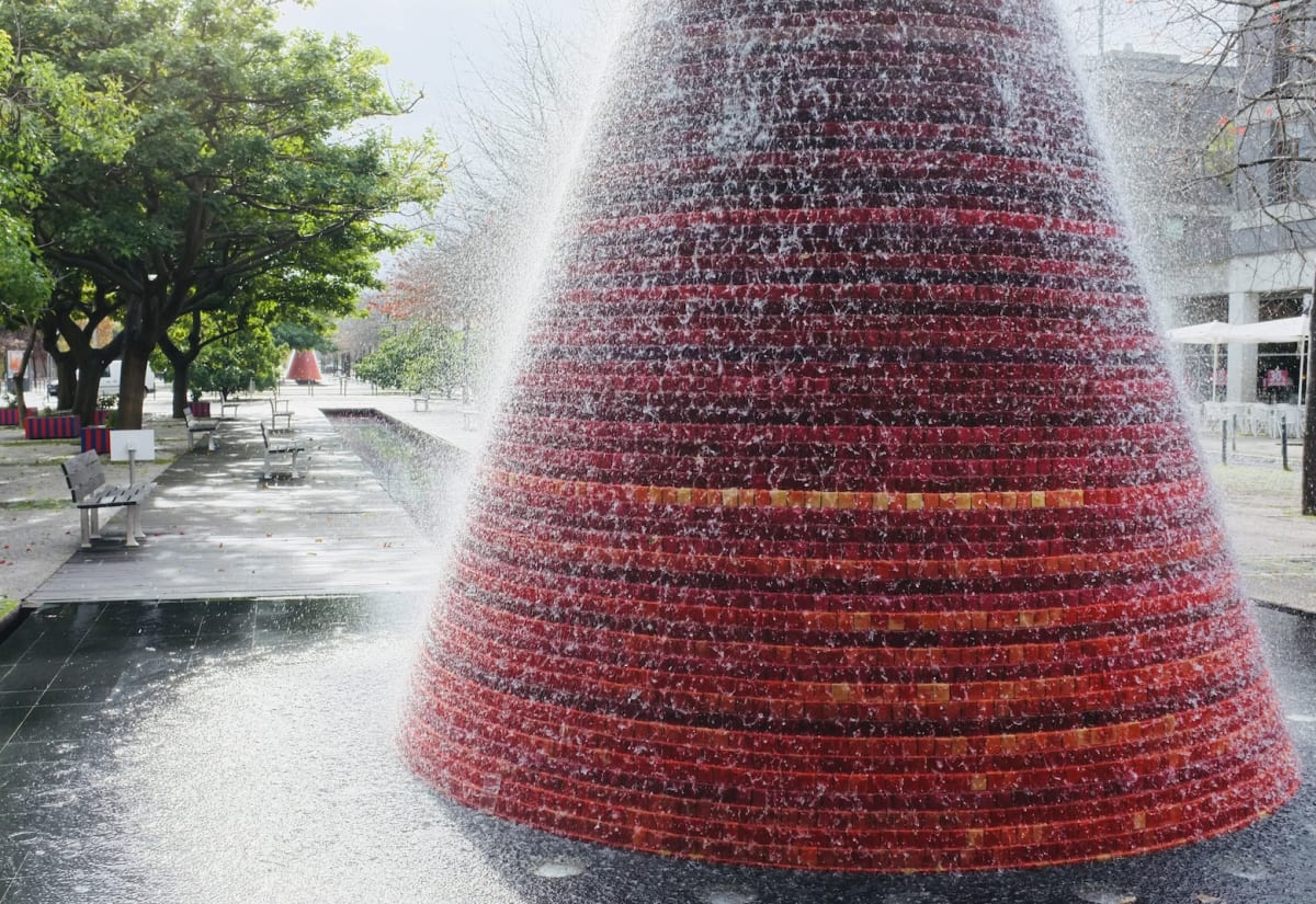 A water fountain in a park, with trees and benches, creating a serene environment in gay Lisbon.