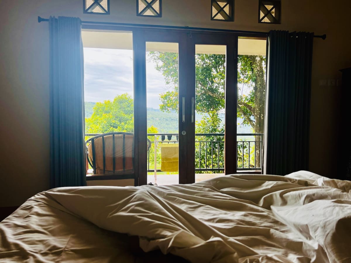 Two figures of people in a hotel bed with a sprawling view of a green rainforest.