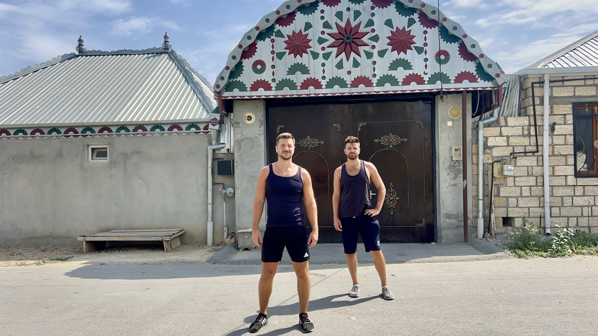 Two men standing in front of a decorative gate with traditional patterns.