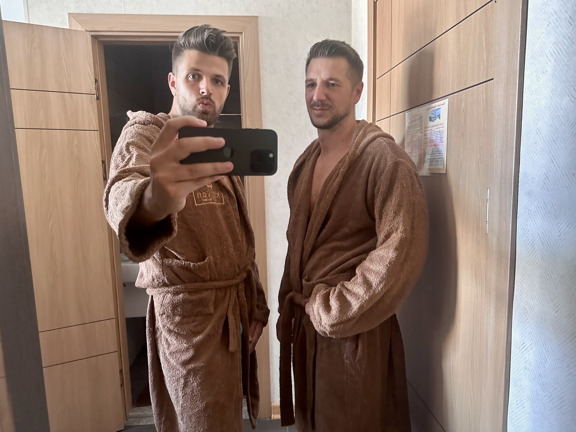 Two individuals in brown robes taking a selfie in front of a mirror.