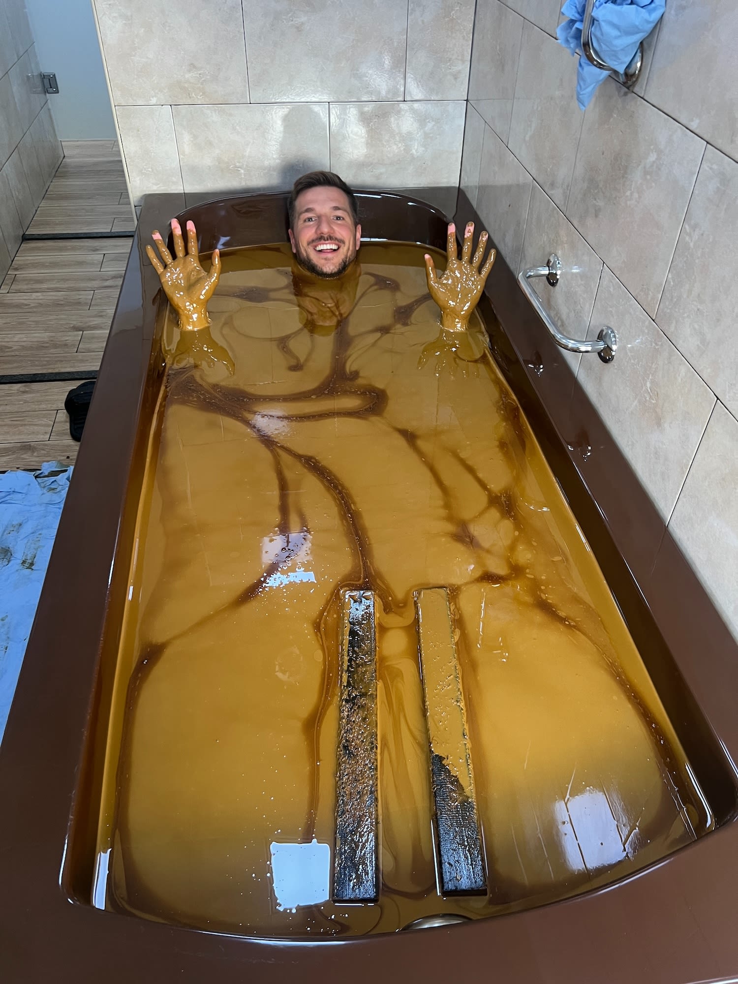 A bathtub filled with a brown, muddy liquid, two visible hands making gestures.