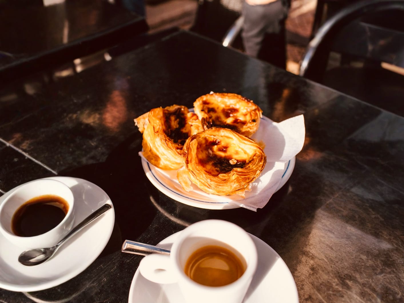 A plate of traditional Portuguese pastries, Pastéis de Nata, served with espresso on a café table in gay Lisbon.