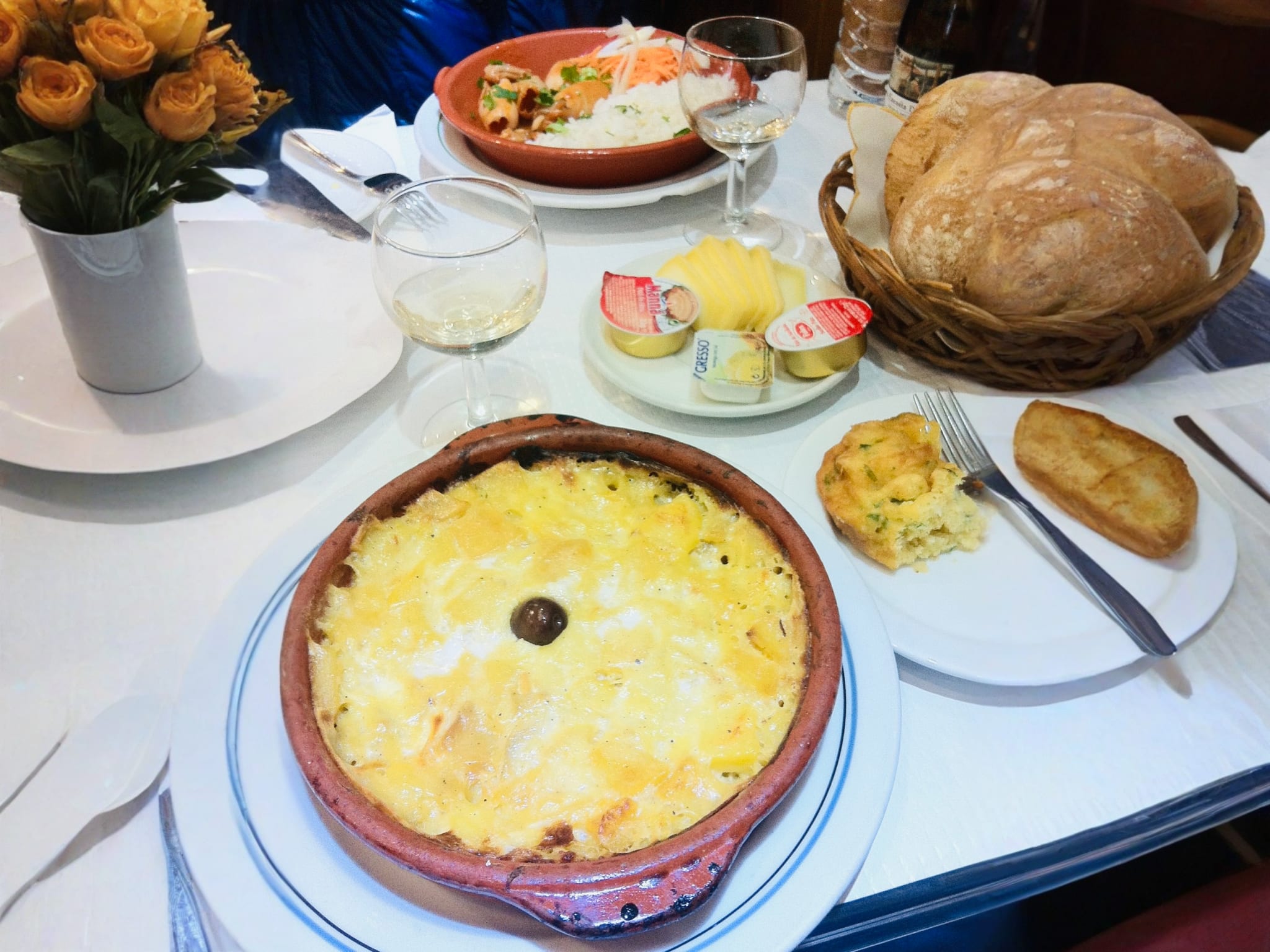 A delicious Portuguese dish, bacalhau, served in a traditional clay pot with sides of bread, butter, and wine, showcasing the culinary delights of gay Lisbon.