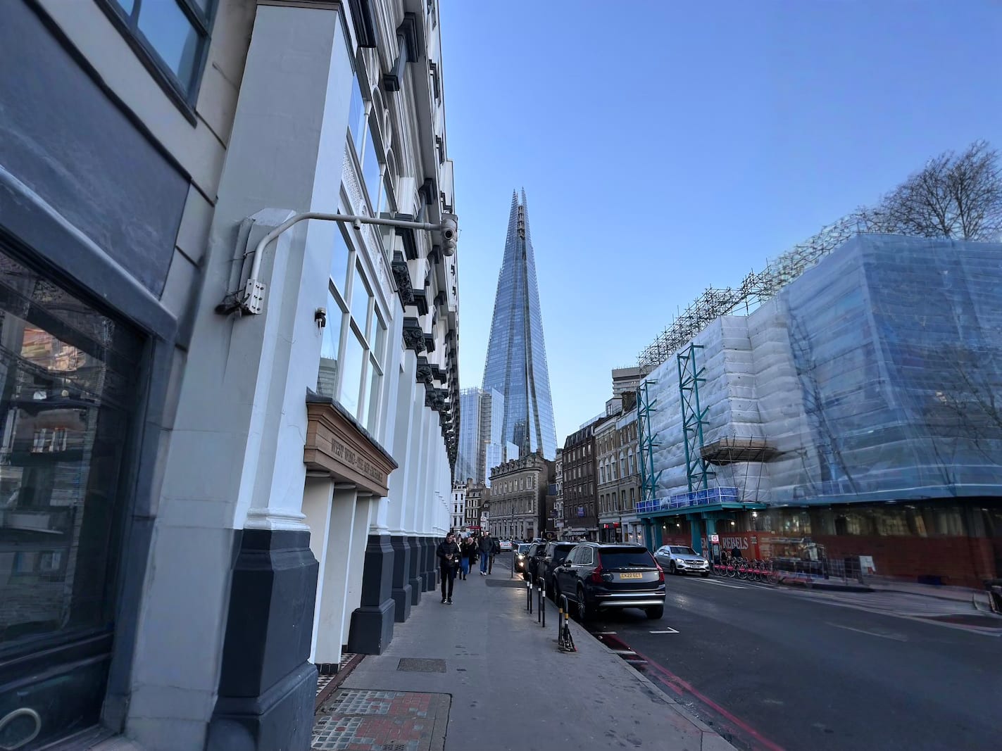 The Shard piercing the blue sky, as seen from a bustling London street, a testament to the city's architectural marvels and Gay London's urban charm.