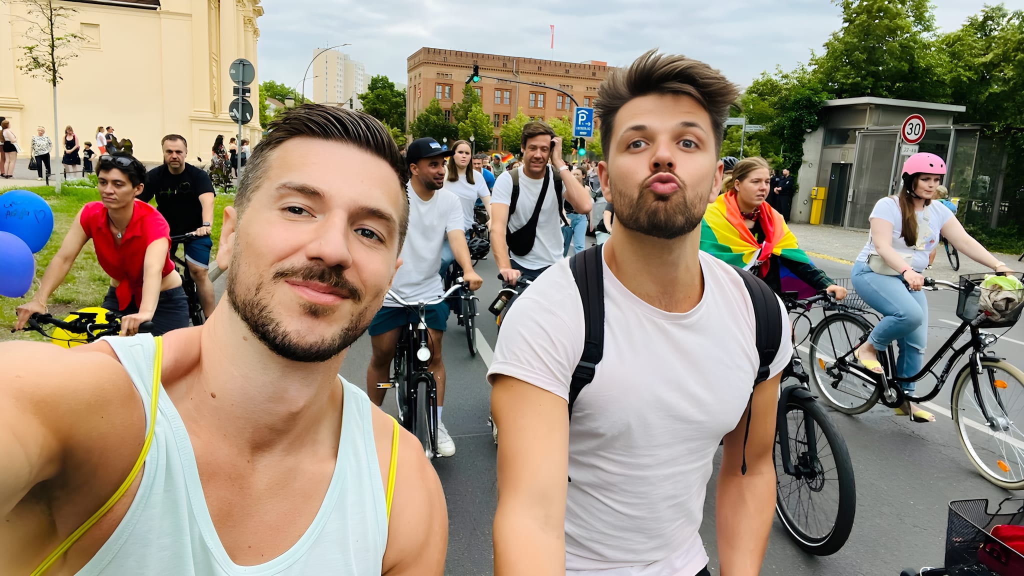 Two joyful men take a selfie in the midst of a vibrant bike parade, showcasing the lively spirit of gay pride in Europe, with participants of all ages cycling and celebrating diversity.