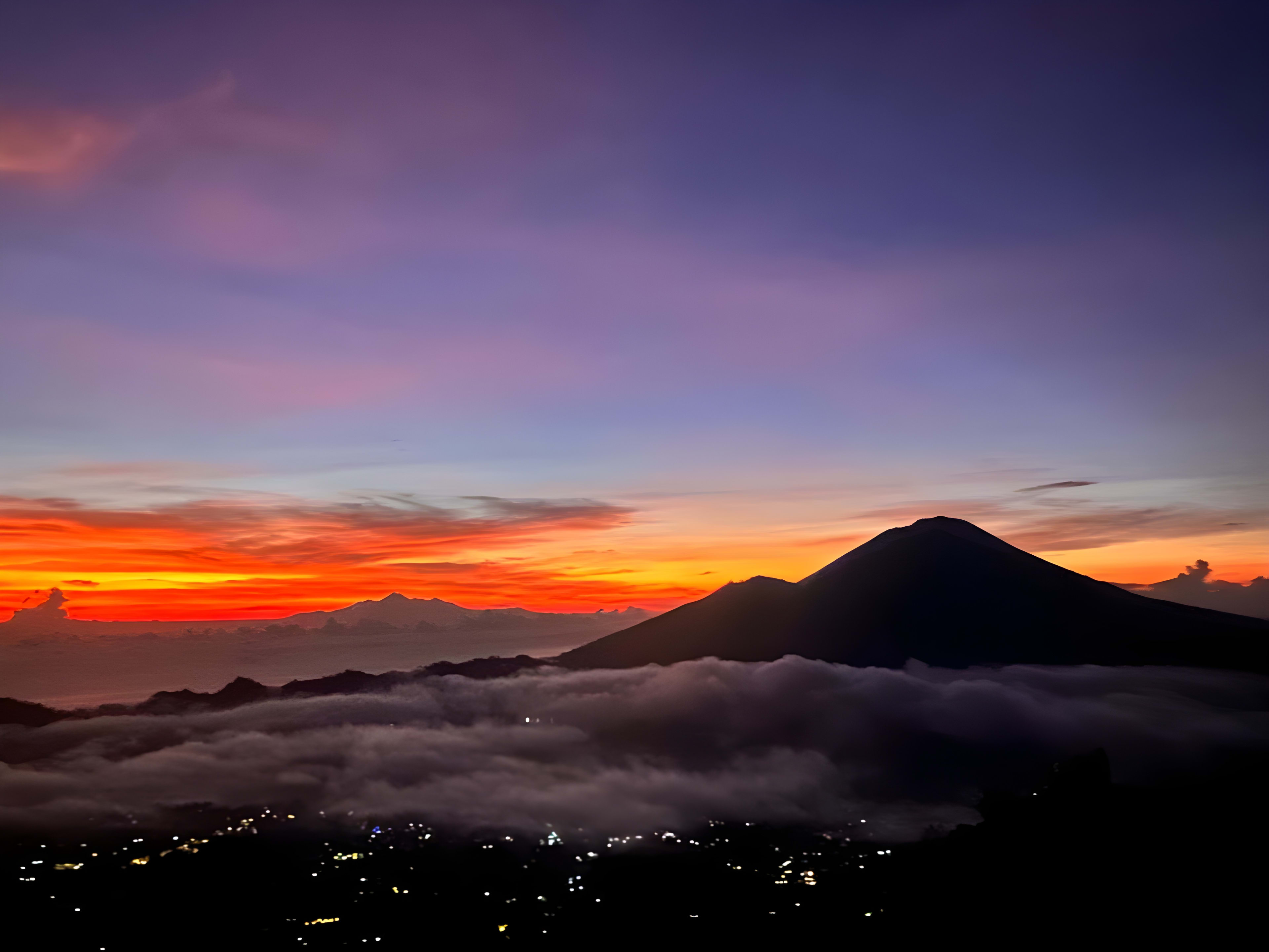 Sunrise view from Mount Batur in Bali, with the sun illuminating the sky in vivid colors and clouds hovering over the volcanic landscape, a magnificent sight for digital nomads.