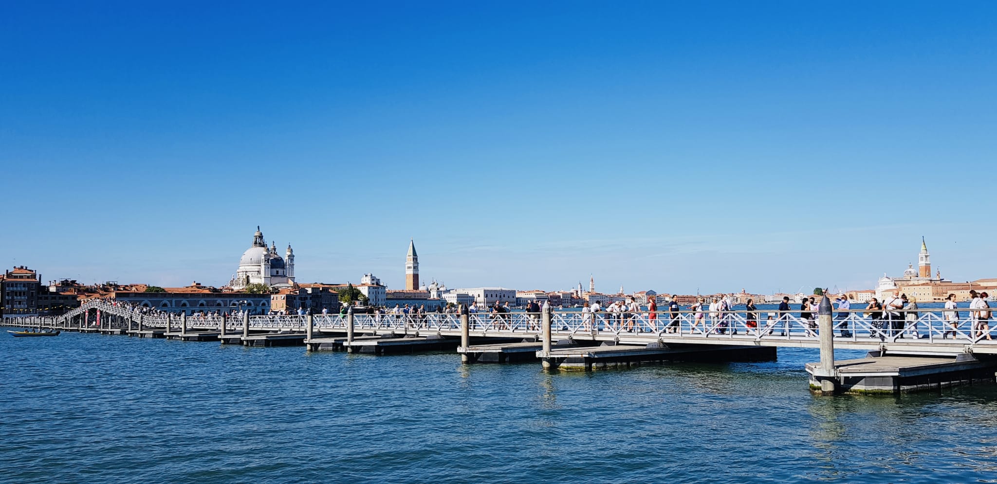 A temporary pedestrian bridge gracefully spans the water in Venice, Italy, set against a backdrop of historical buildings and a clear blue sky.