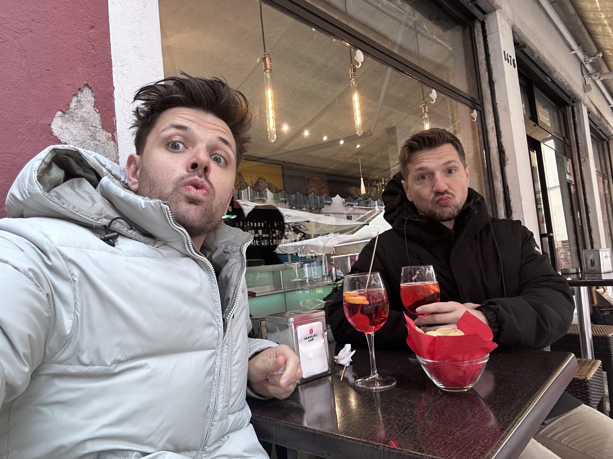 Two people sit at an outdoor cafe adorned with vibrant tableware, deep in conversation as they plan their 2 day Venice itinerary. With refreshing cocktails and authentic Venetian dishes beside them, their playful expressions capture the excitement of exploring landmarks like St. Mark's Basilica and the Grand Canal, all amidst a lively atmosphere filled with local charm.