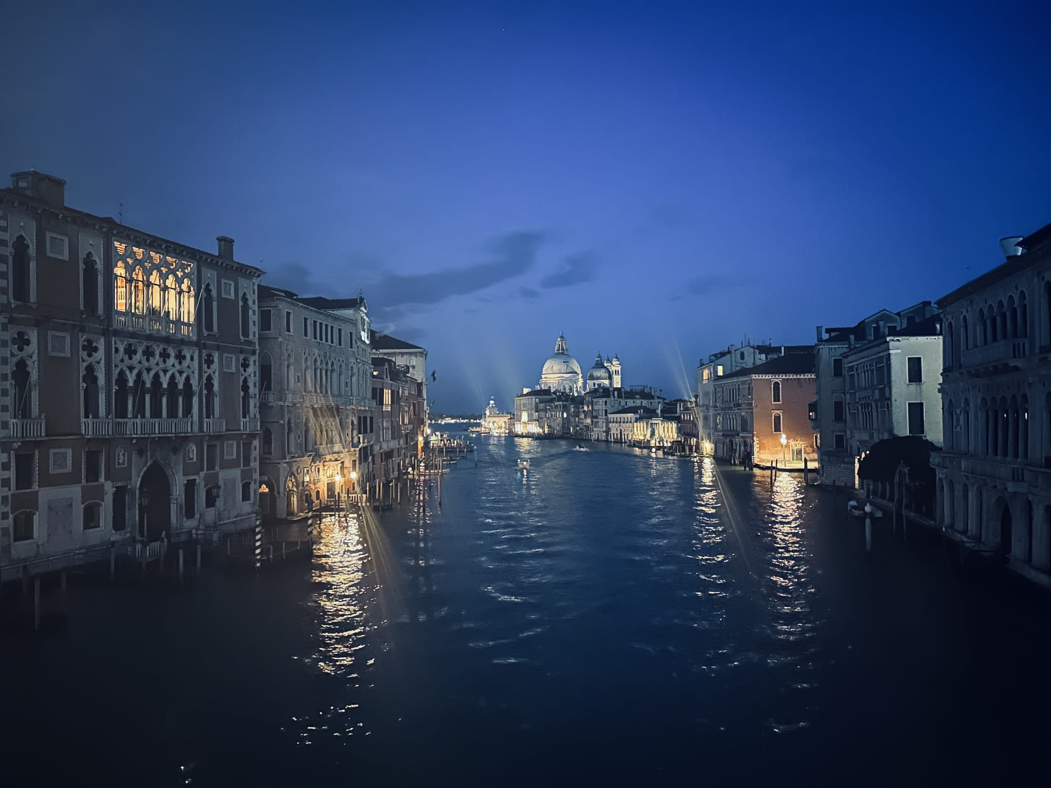 A nighttime view of Venice's Grand Canal showcases illuminated historic buildings and a majestic church dome under a dark blue sky. This iconic scene is ideal for your 2 day Venice itinerary, capturing the essence of Venetian history and architecture, perfect for evening explorations and soaking in the romantic ambiance of this enchanting city.