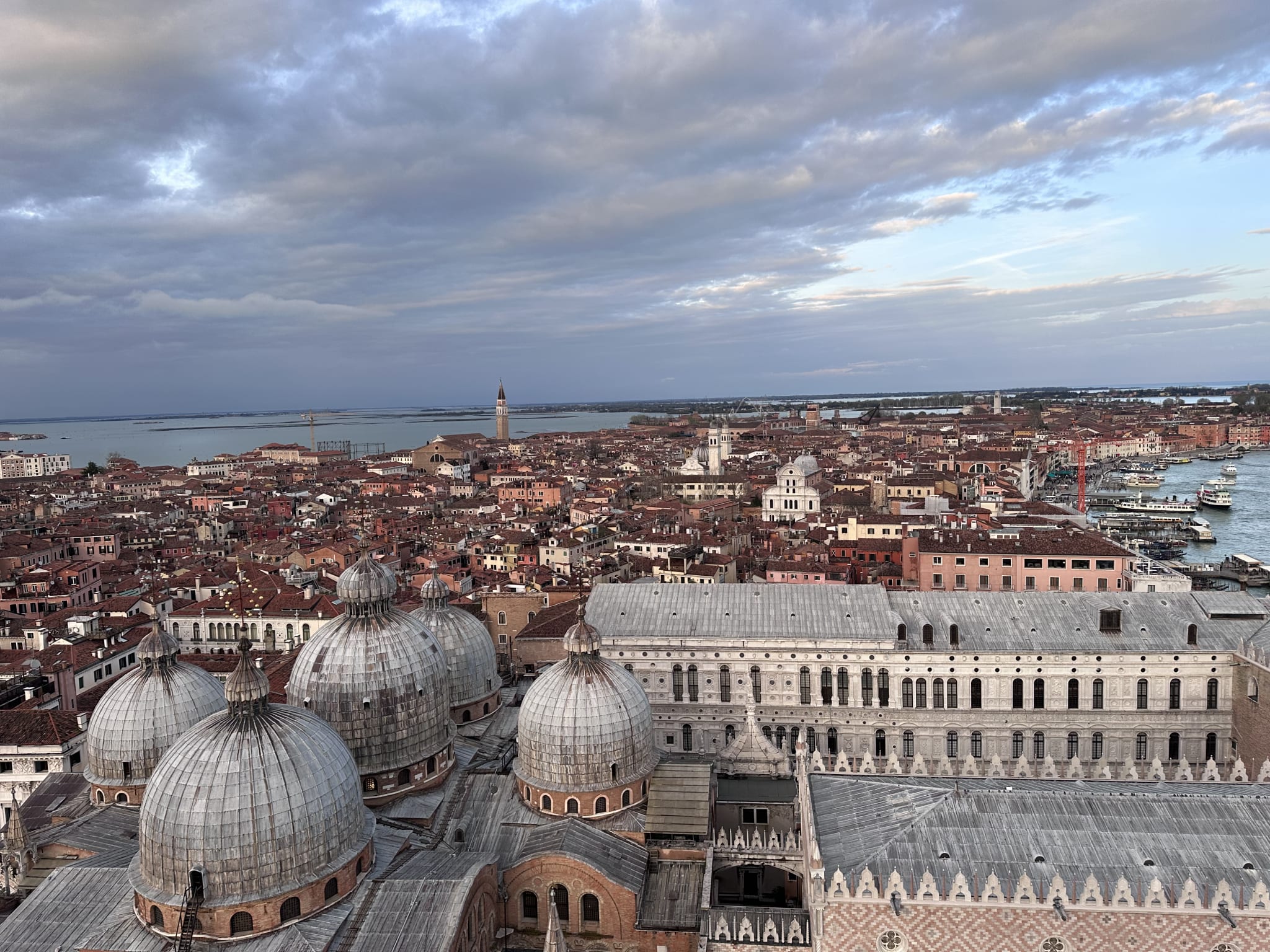Aerial view captures the enchanting beauty of Venice, highlighting the majestic domes of a cathedral against a backdrop of historic buildings and winding canals beneath a cloudy sky. Ideal for exploring over 2 days, this scene offers an inspiring glimpse into what could be a memorable 2 day Venice itinerary, showcasing key landmarks and the city's unique charm.