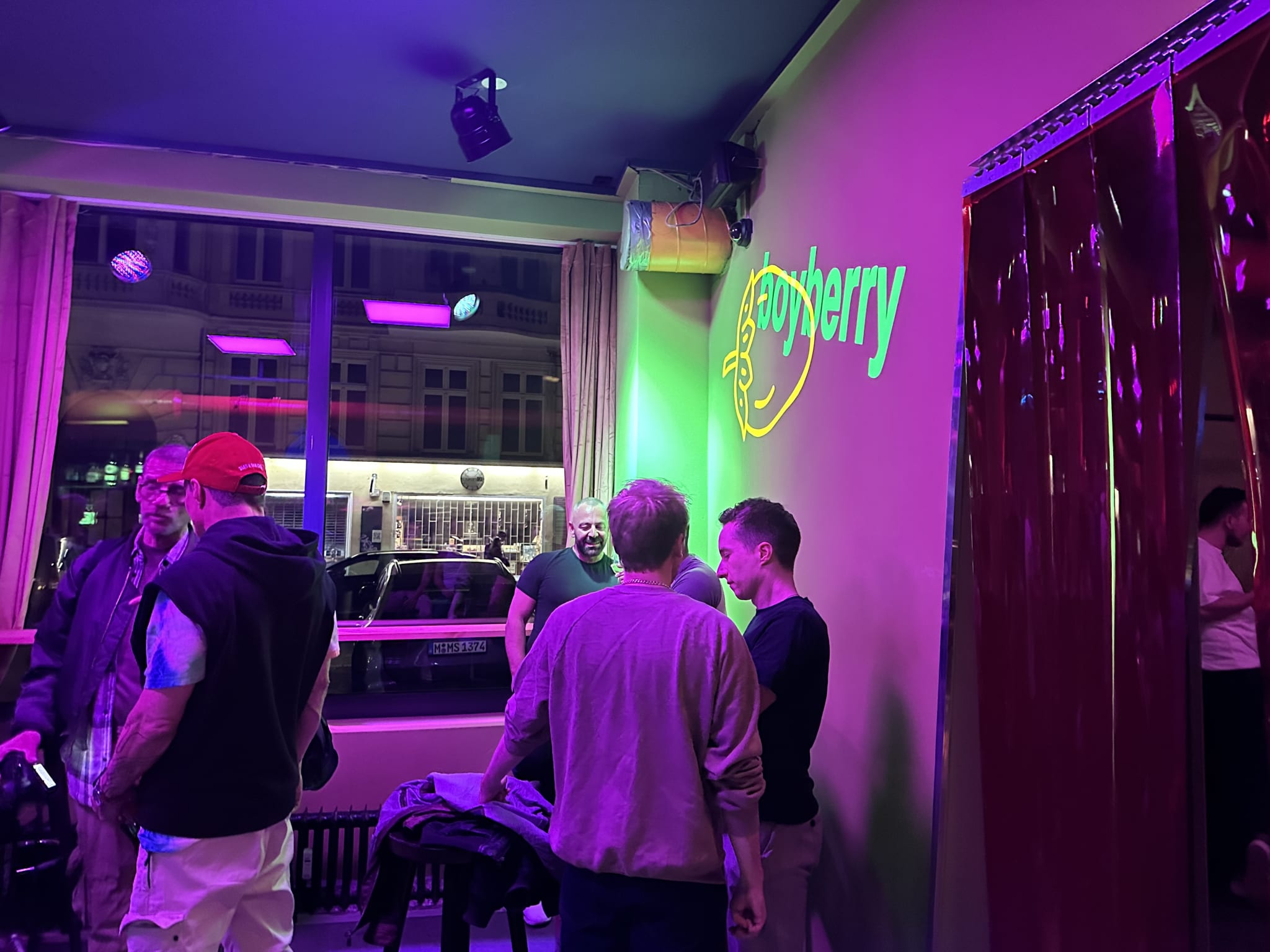 Patrons socialize under neon lights at Boyberry, a lively destination contributing to Berlin's gay nightlife scene, with the club's neon sign casting a warm glow over the crowd.