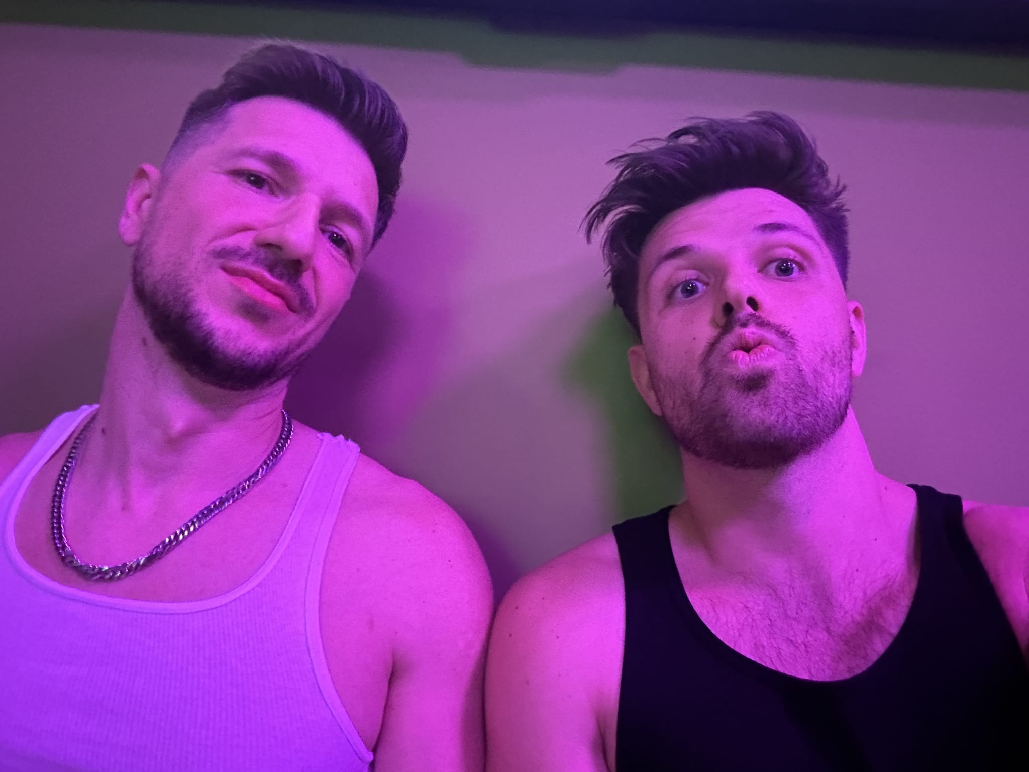 Two smiling men enjoying Berlin's vibrant gay nightlife, playfully posing under purple lighting at Boyberry, a popular local hangout.