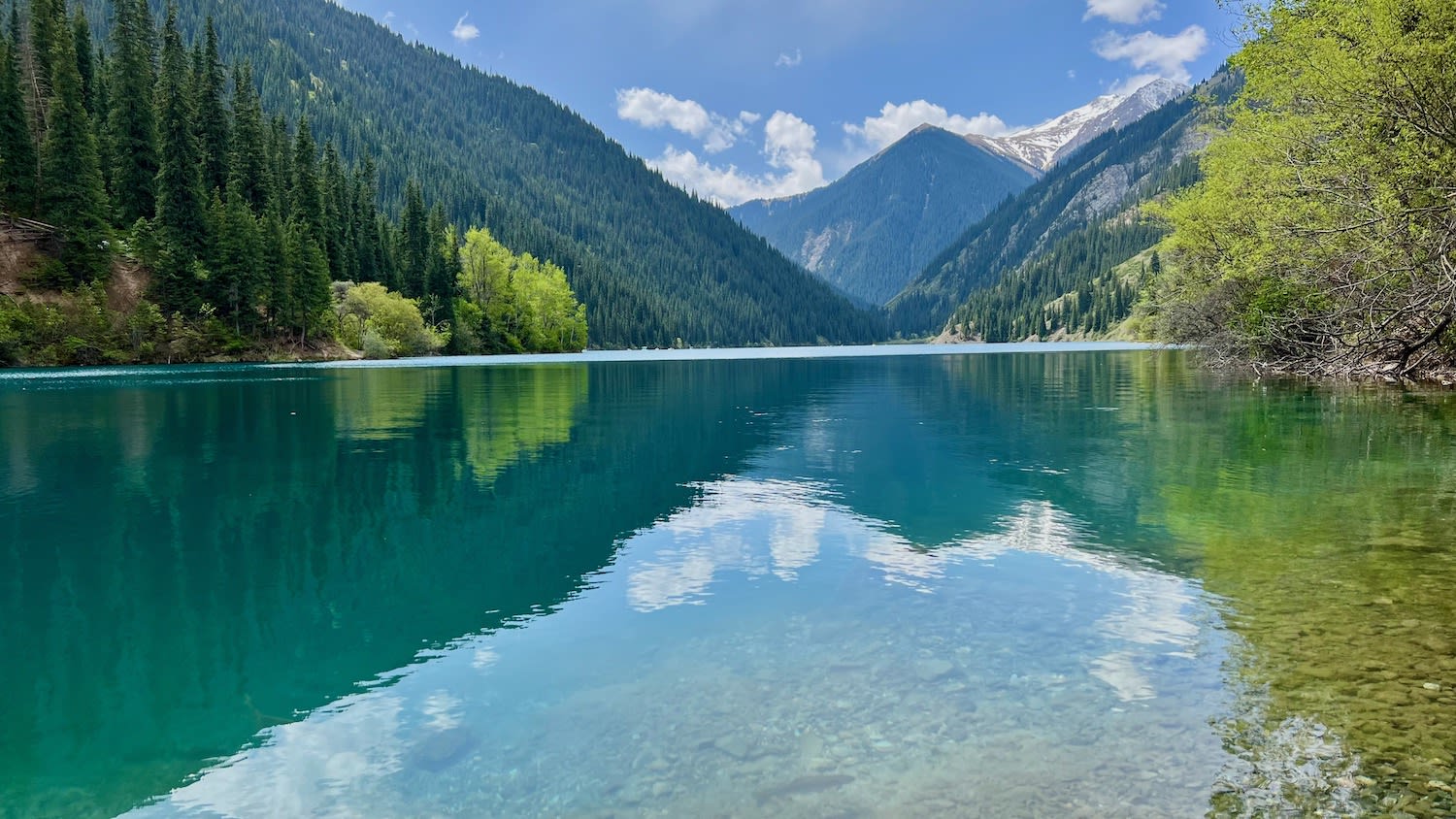 Tranquil Kolsai Lake reflecting the surrounding pine forests and snow-dusted mountains, epitomizing the natural beauty encountered while traveling in Kazakhstan.