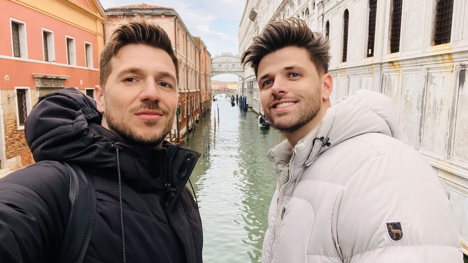 Two individuals snapping a selfie on a charming Venetian bridge, surrounded by iconic narrow canals and historic buildings. This memorable moment is part of their 2 day Venice itinerary, capturing the essence of the city's enchanting beauty and timeless architecture as they explore its picturesque scenery.
