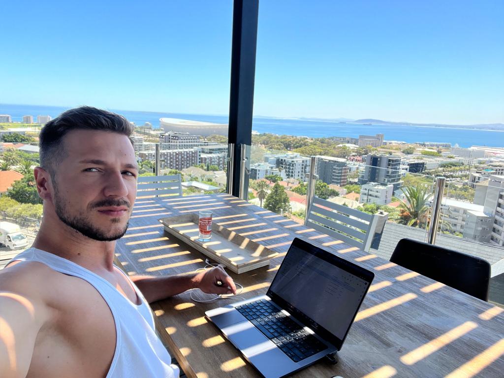 A young man working on his laptop at a high-rise balcony overlooking Cape Town, [South Africa](/destinations/south-africa), demonstrating the lifestyle of digital nomads using affordable VPNs to securely access the internet from anywhere.