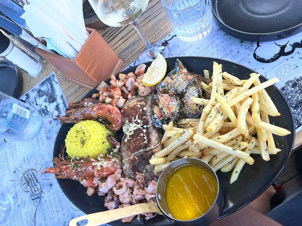 A lavish seafood platter featuring prawns, squid, and grilled fish, served with sides of yellow rice and fries, enjoyed at an outdoor eatery in Cape Town, a popular choice for digital nomads looking to experience local cuisine.