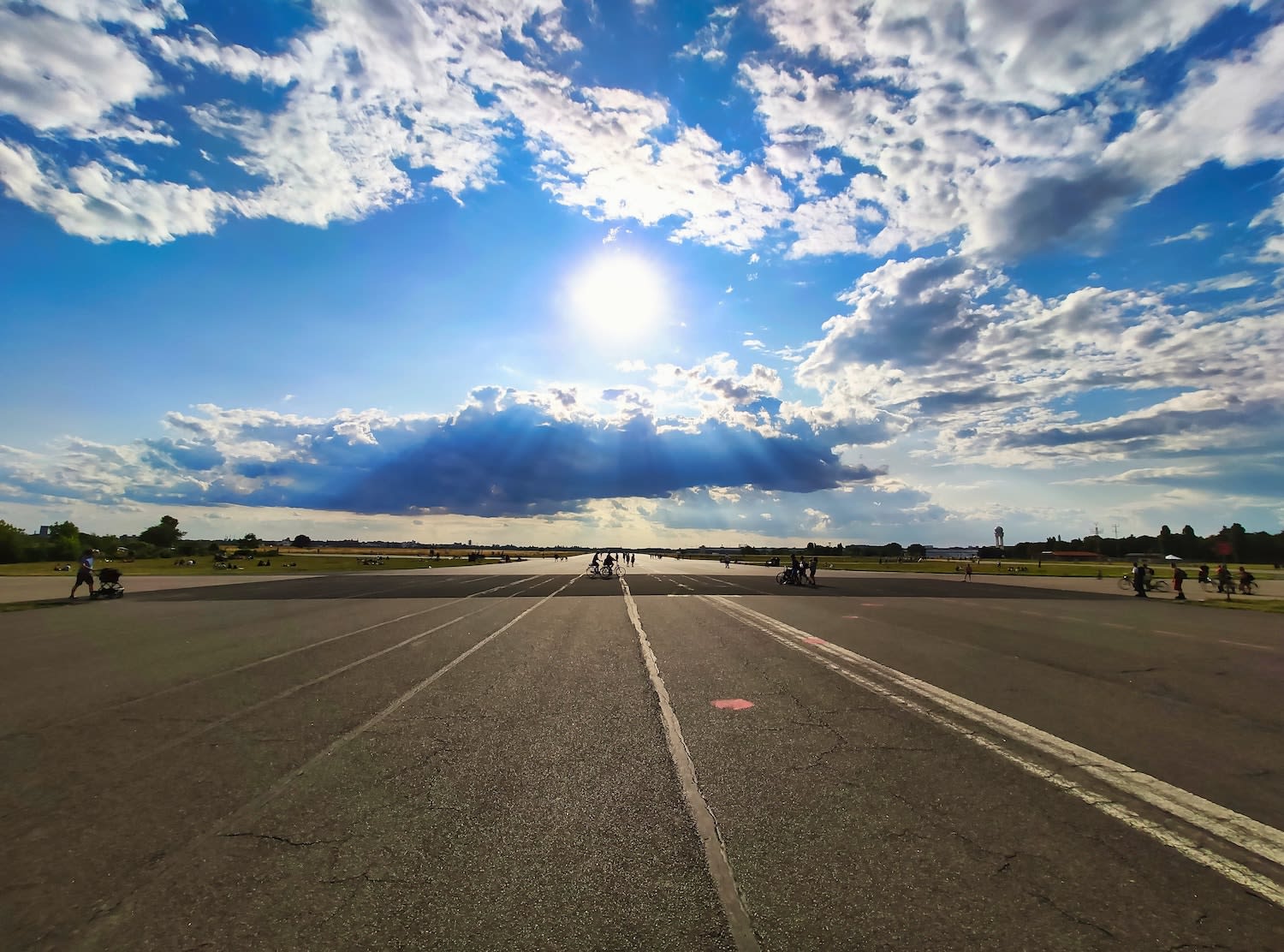 People enjoying various activities on the wide, expansive runway of Tempelhofer Feld in Berlin under a dramatic sky, illustrating the site's transformation into a unique urban park.