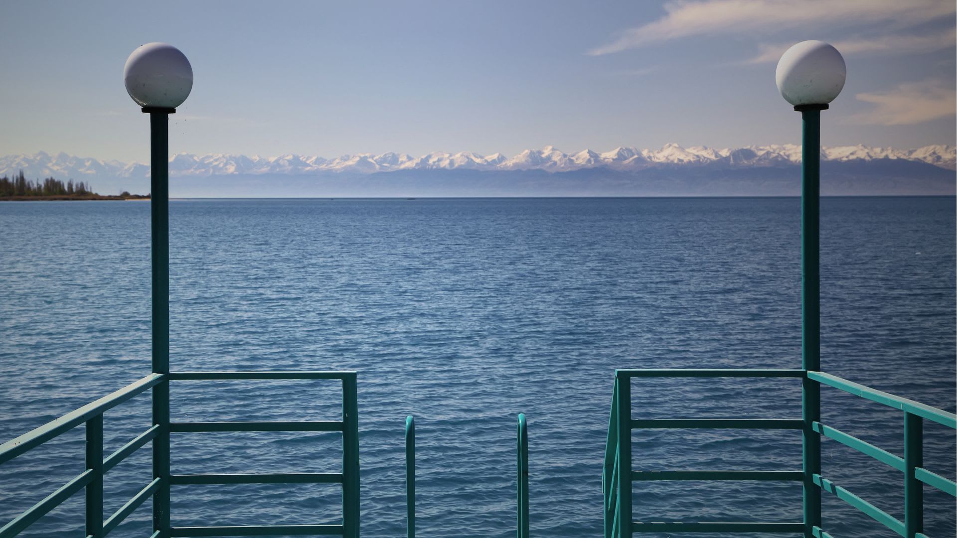 Scenic view from a pier at Lake Issyk-Kul, Kyrgyzstan, with snow-capped mountains in the distance and a clear blue sky, a peaceful retreat not far from Bishkek.