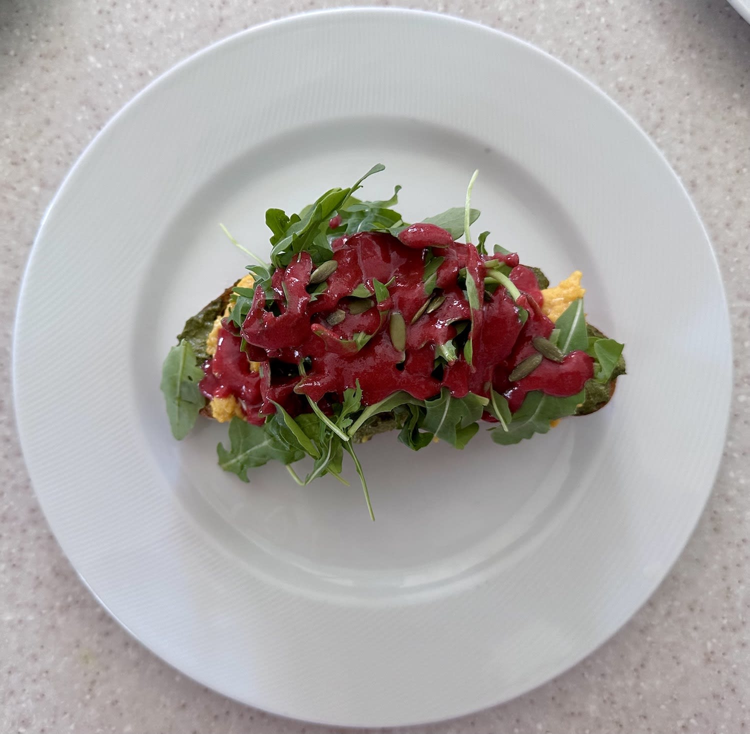 A healthy breakfast plate featuring arugula, red sauce, seeds, and greens on a white dish.