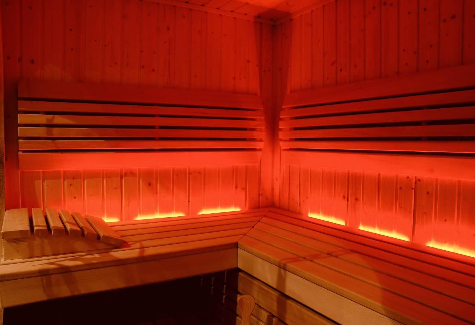 A gay sauna with warm red lighting, wooden benches, and a cozy, inviting atmosphere, perfect for relaxation.