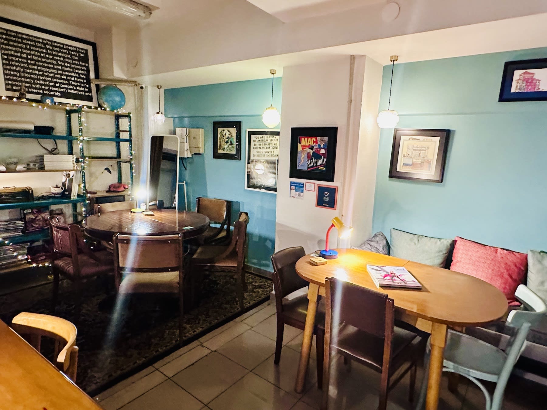 A cozy indoor space at The Caravan, featuring wooden tables, eclectic decor, and warm lighting. The area includes bookshelves, framed artwork, and comfortable seating for a relaxed work or social environment.
