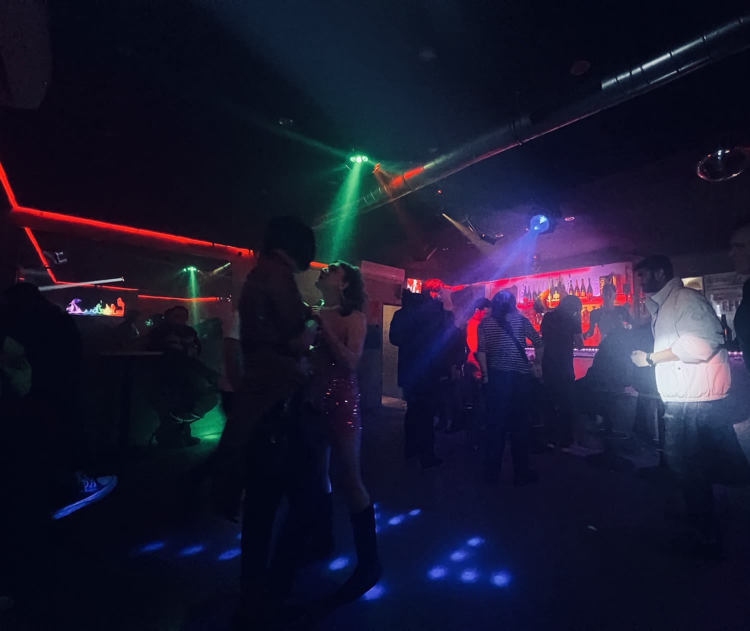 Vibrant nightlife scene in a gay Frankfurt club (Comeback) with people dancing under red and green lights, illustrating the city's inclusive and dynamic LGBTQ community.