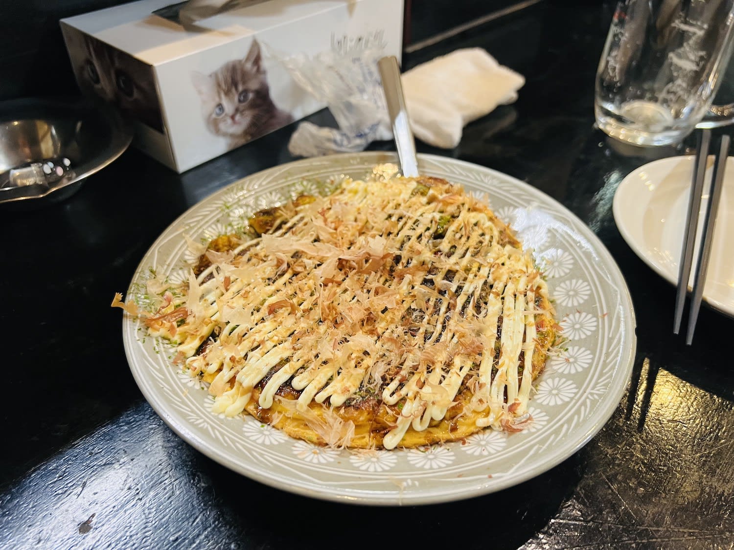 Traditional Okonomiyaki, a Japanese savory pancake, topped with bonito flakes and mayonnaise, served on a ceramic plate in a Nagasaki eatery. It is something to try during a Nagasaki itinerary.