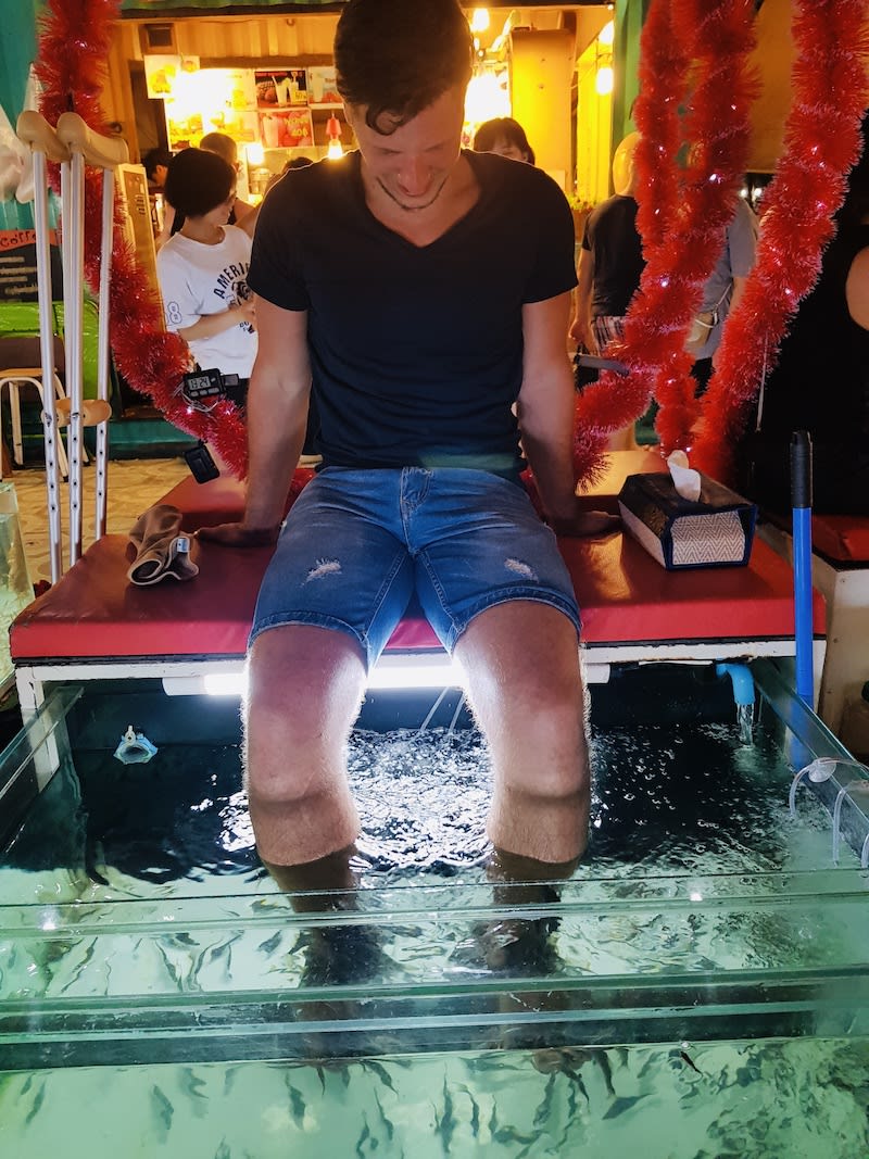 Man experiencing a fish spa treatment in Phuket, a unique activity on a 14 day Thailand journey.