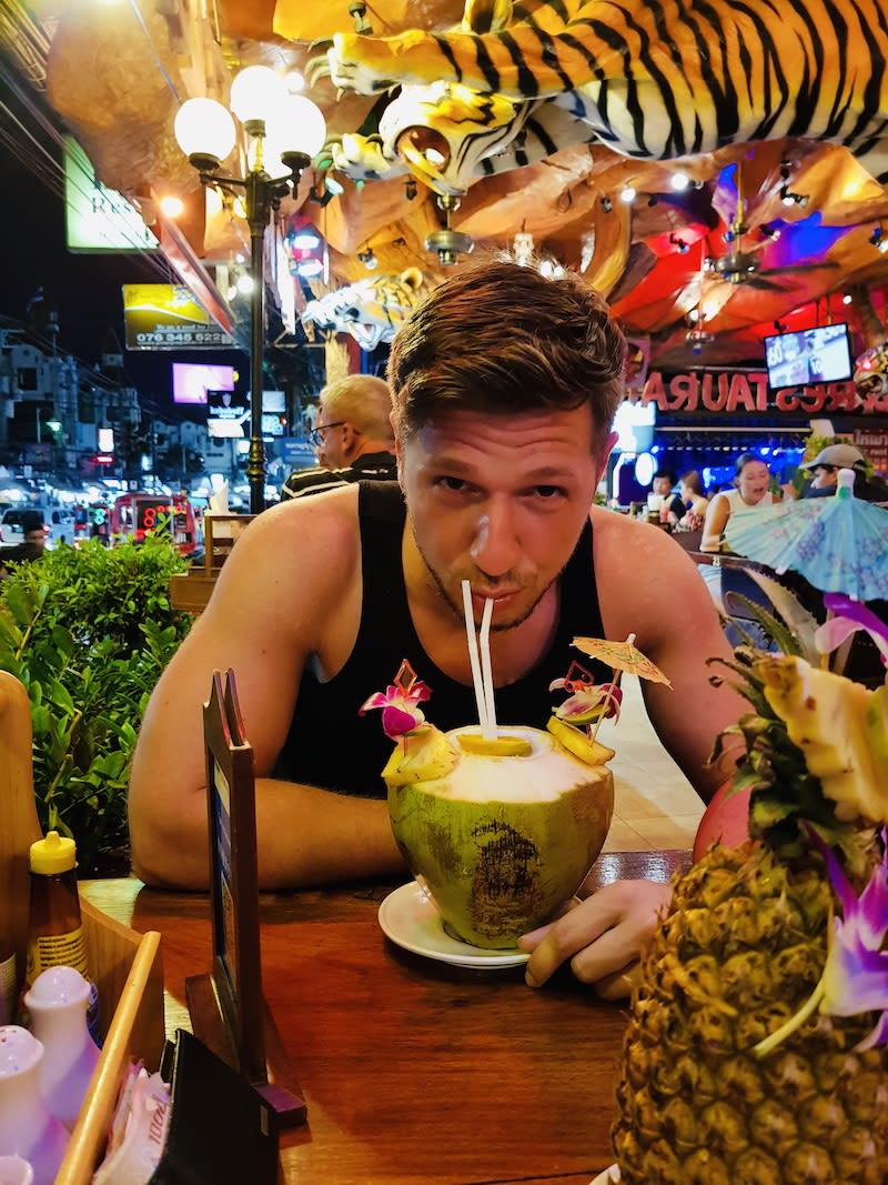Tourist enjoying a fresh coconut drink at a Phuket bar, a tropical delight on a 14 day Thailand itinerary.