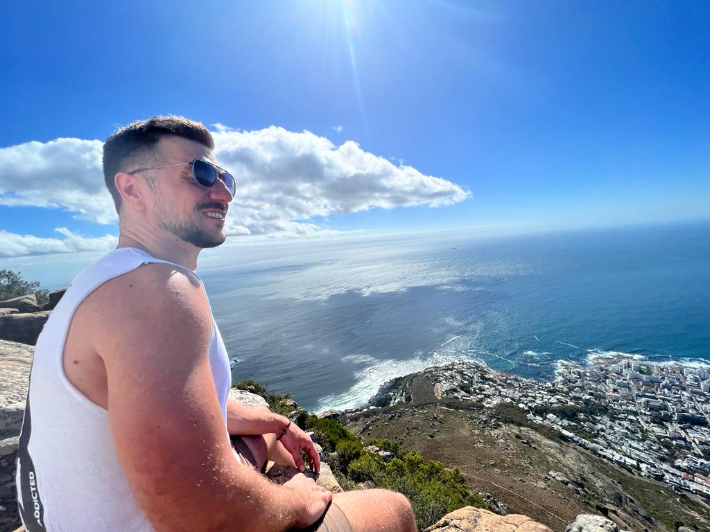 A digital nomad enjoying a break with a scenic view over Cape Town from the top of Lion's Head mountain, showcasing the blend of adventure and work.